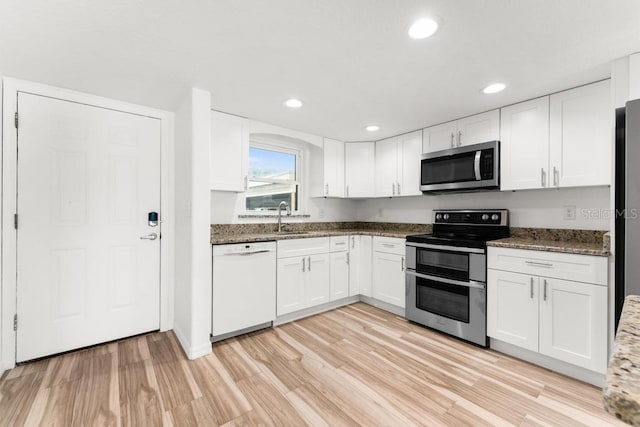 kitchen featuring white cabinets, light wood-type flooring, appliances with stainless steel finishes, and dark stone counters