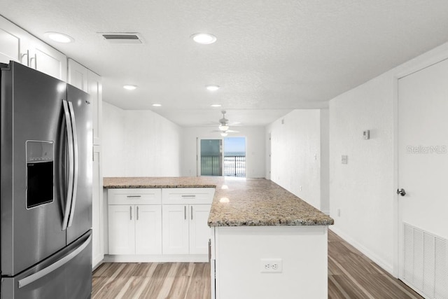 kitchen featuring white cabinetry, stainless steel fridge, light hardwood / wood-style flooring, and light stone countertops