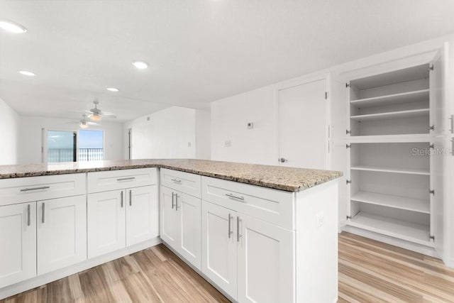 kitchen with white cabinets, ceiling fan, light stone countertops, and light wood-type flooring