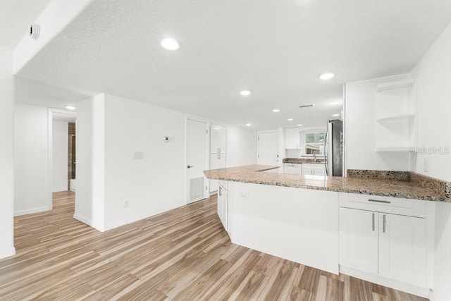 kitchen with kitchen peninsula, light wood-type flooring, stone countertops, white cabinets, and stainless steel refrigerator