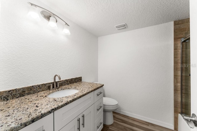 bathroom featuring hardwood / wood-style floors, vanity, toilet, a textured ceiling, and a shower with shower door