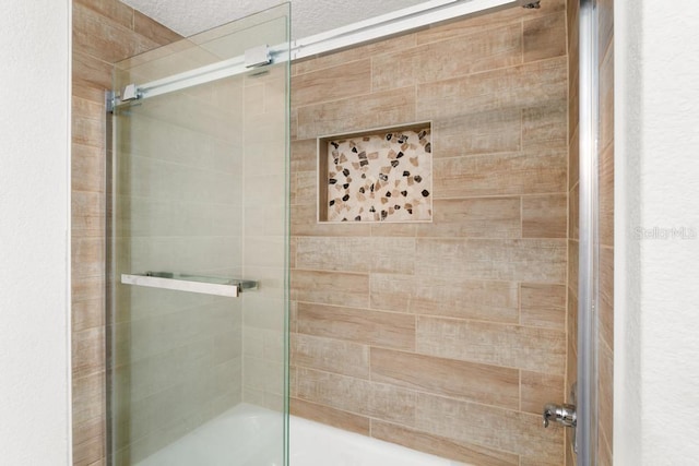 bathroom with combined bath / shower with glass door and a textured ceiling