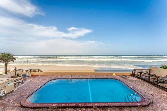 view of pool featuring a patio area, a water view, and a view of the beach