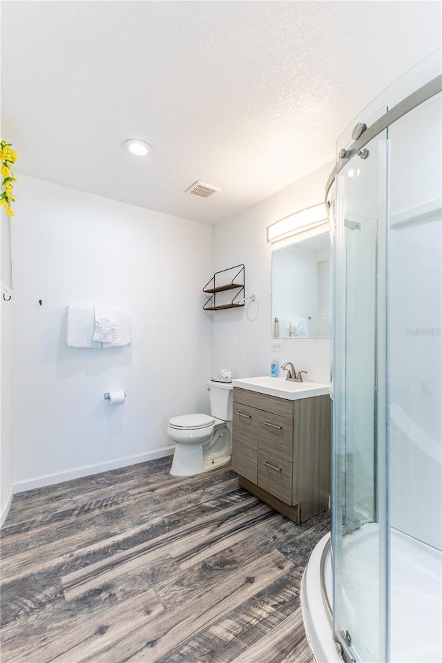 bathroom featuring hardwood / wood-style floors, vanity, toilet, walk in shower, and a textured ceiling