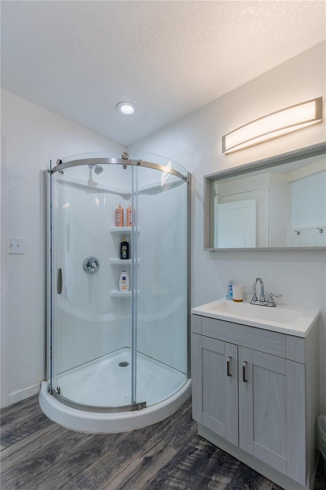 bathroom with a textured ceiling, vanity, wood-type flooring, and an enclosed shower