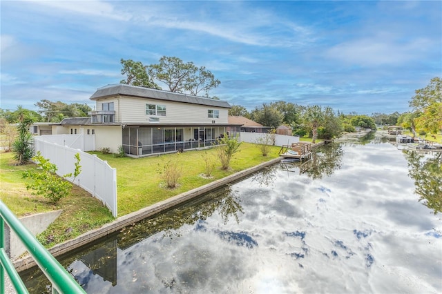 rear view of house with a sunroom, a yard, and a water view