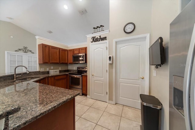 kitchen with dark stone counters, sink, vaulted ceiling, light tile patterned floors, and stainless steel appliances