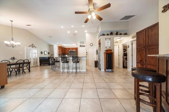 kitchen with a kitchen breakfast bar, ceiling fan with notable chandelier, stainless steel appliances, hanging light fixtures, and light tile patterned flooring