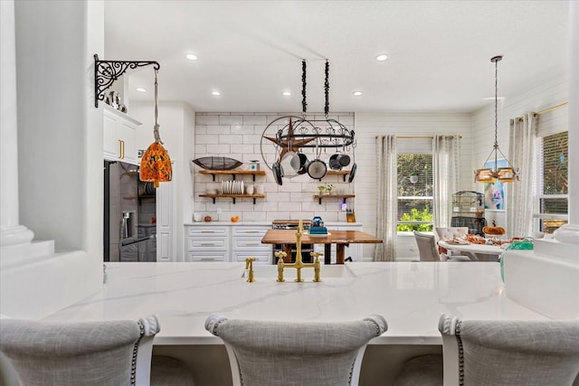 kitchen with a breakfast bar, pendant lighting, white cabinets, stainless steel fridge, and light stone countertops