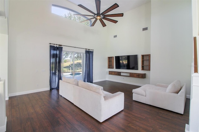 living room with dark hardwood / wood-style flooring, a towering ceiling, and ceiling fan