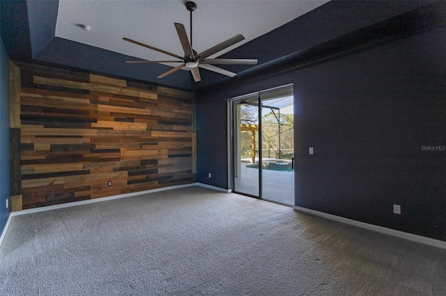 carpeted empty room featuring a tray ceiling, wooden walls, and ceiling fan