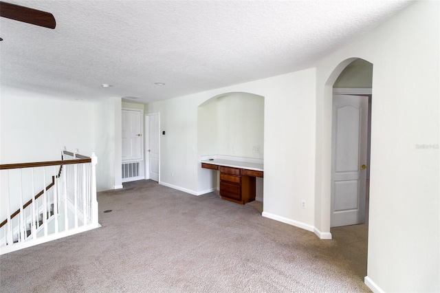 spare room with built in desk, light carpet, and a textured ceiling