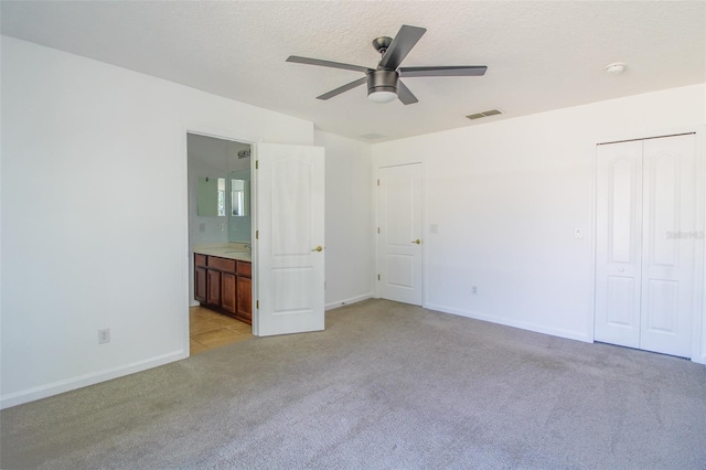 unfurnished bedroom with connected bathroom, sink, light colored carpet, a textured ceiling, and ceiling fan