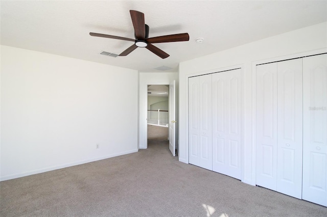 unfurnished bedroom featuring light carpet, two closets, and ceiling fan