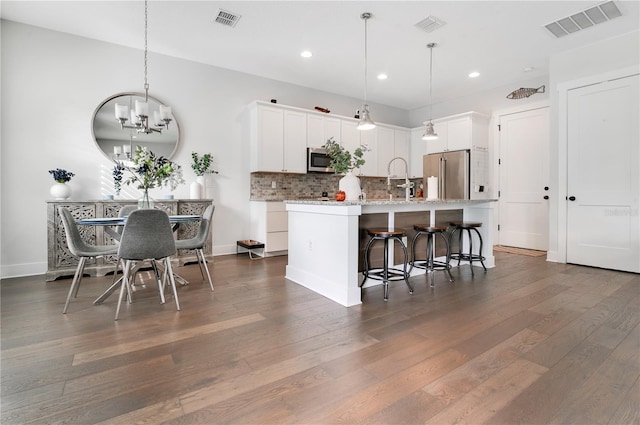 kitchen with hanging light fixtures, stainless steel appliances, dark hardwood / wood-style flooring, a center island with sink, and white cabinets