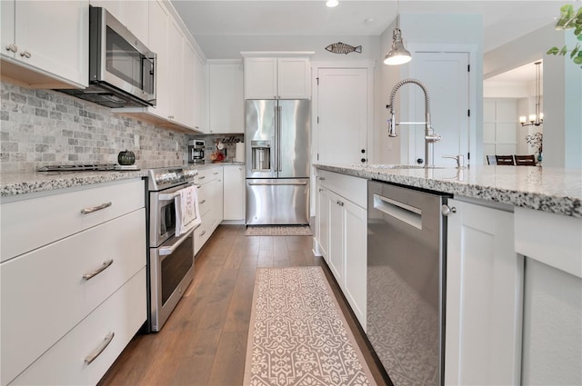 kitchen featuring light stone countertops, premium appliances, hardwood / wood-style floors, pendant lighting, and white cabinets