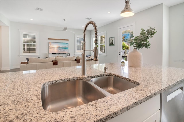 kitchen with light stone counters, stainless steel dishwasher, sink, decorative light fixtures, and white cabinetry