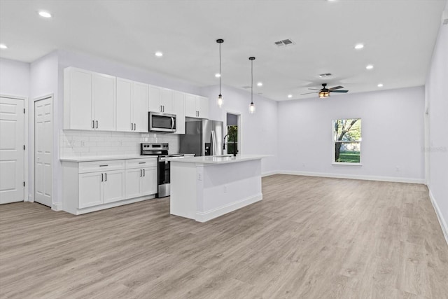 kitchen with appliances with stainless steel finishes, light wood-type flooring, a kitchen island with sink, decorative light fixtures, and white cabinetry