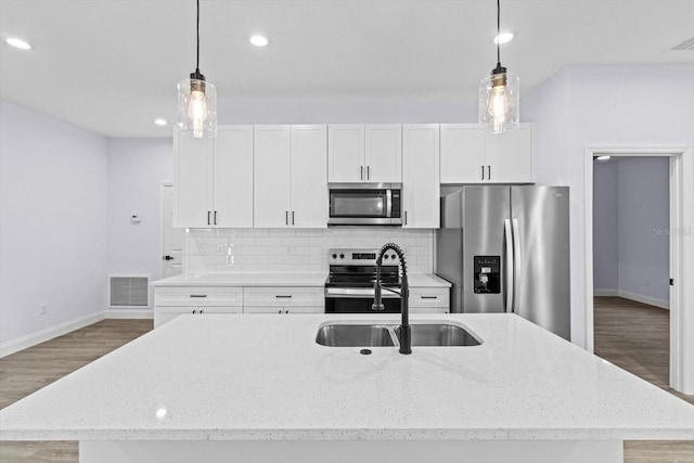 kitchen featuring a center island with sink, stainless steel appliances, decorative light fixtures, and wood-type flooring