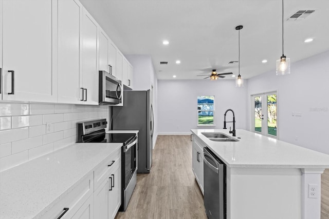 kitchen with appliances with stainless steel finishes, ceiling fan, a kitchen island with sink, sink, and light hardwood / wood-style floors