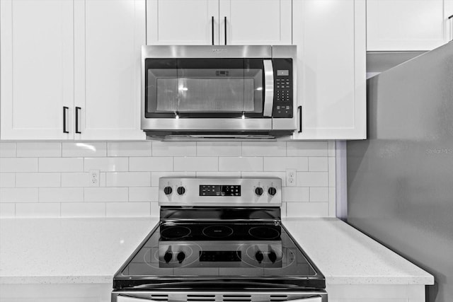 kitchen with white cabinets, light stone countertops, backsplash, and appliances with stainless steel finishes