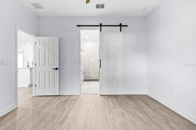 unfurnished bedroom featuring a barn door, ensuite bathroom, sink, and light hardwood / wood-style floors