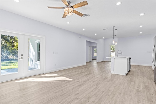 kitchen featuring pendant lighting, french doors, sink, light hardwood / wood-style flooring, and an island with sink