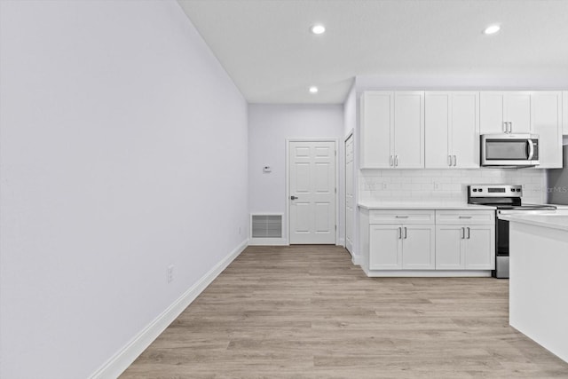 kitchen with white cabinets, backsplash, light hardwood / wood-style floors, and stainless steel appliances