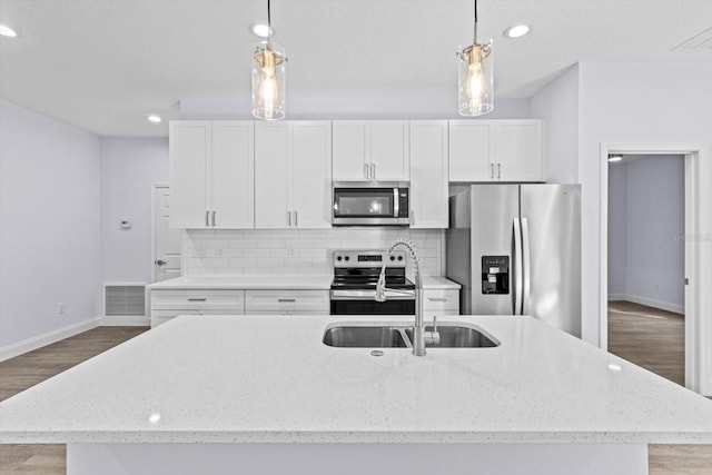 kitchen featuring light stone counters, stainless steel appliances, a center island with sink, white cabinets, and hanging light fixtures