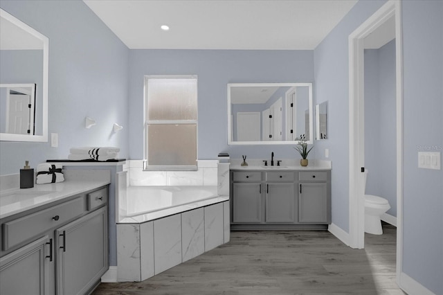 bathroom featuring hardwood / wood-style floors, vanity, toilet, and tiled tub