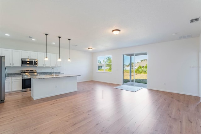 kitchen featuring appliances with stainless steel finishes, light stone counters, pendant lighting, white cabinetry, and an island with sink