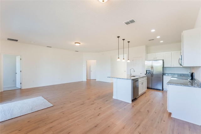 kitchen with appliances with stainless steel finishes, sink, white cabinets, hanging light fixtures, and an island with sink