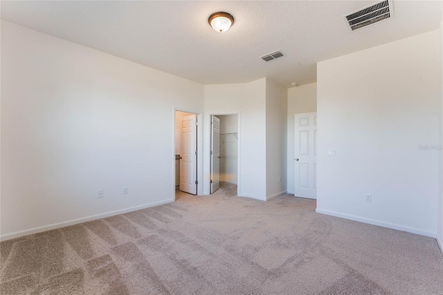 unfurnished bedroom featuring a walk in closet, a closet, and light colored carpet