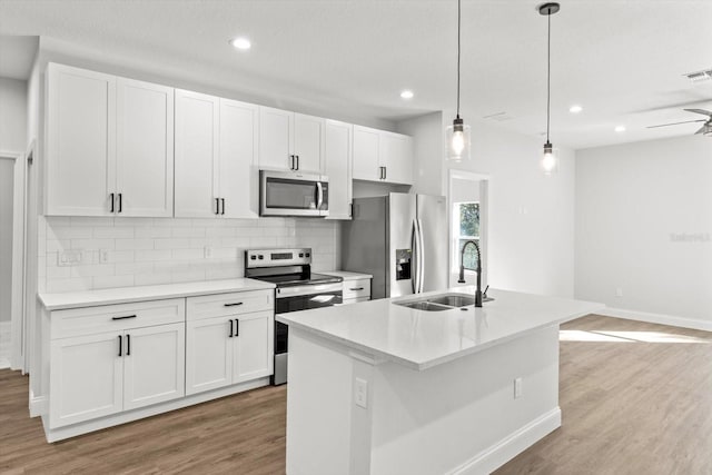 kitchen with pendant lighting, stainless steel appliances, white cabinetry, and a center island with sink