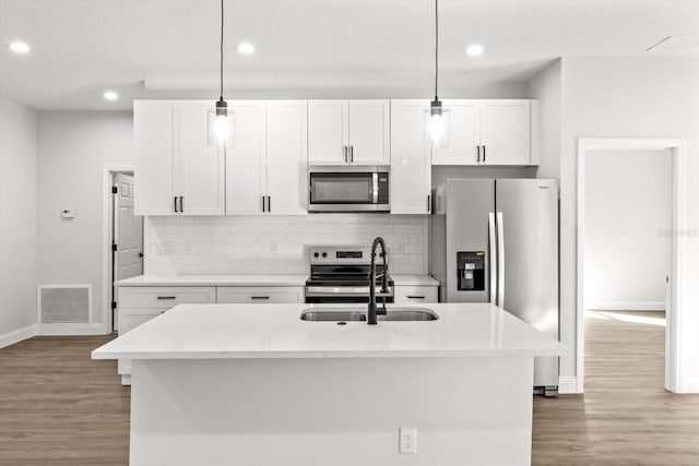 kitchen with light stone countertops, appliances with stainless steel finishes, hanging light fixtures, and an island with sink