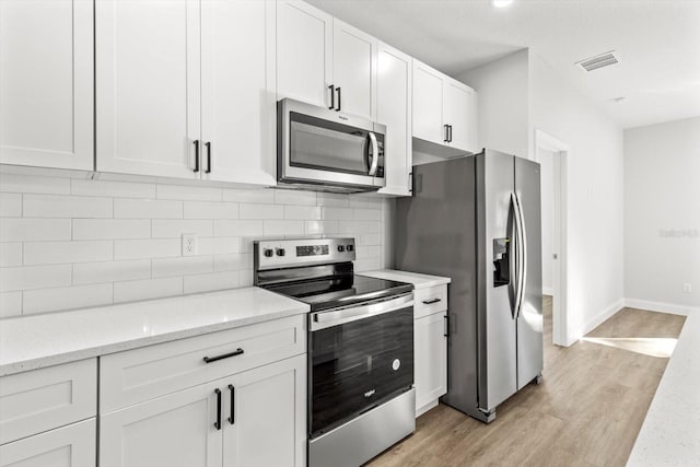 kitchen with light stone counters, light wood-type flooring, white cabinetry, and stainless steel appliances