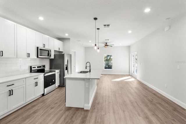 kitchen featuring stainless steel appliances, ceiling fan, sink, pendant lighting, and an island with sink