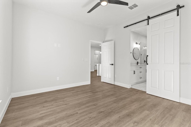 unfurnished bedroom with a barn door, ensuite bathroom, ceiling fan, and wood-type flooring