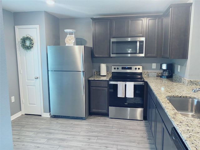 kitchen with dark brown cabinetry, light stone countertops, sink, stainless steel appliances, and light hardwood / wood-style floors