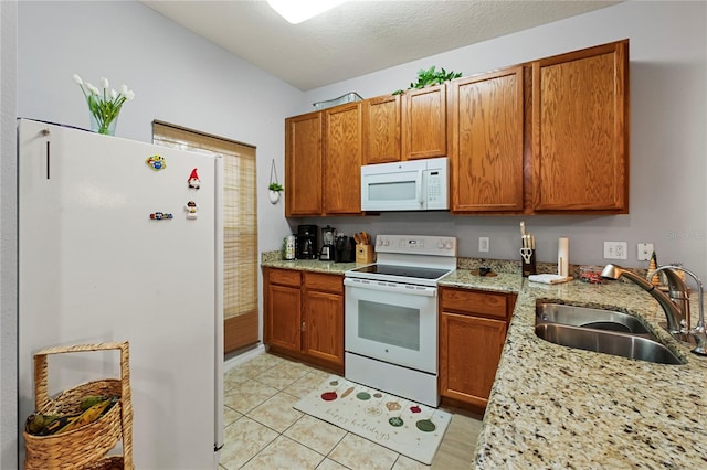 kitchen featuring light stone countertops, sink, a textured ceiling, white appliances, and light tile patterned floors