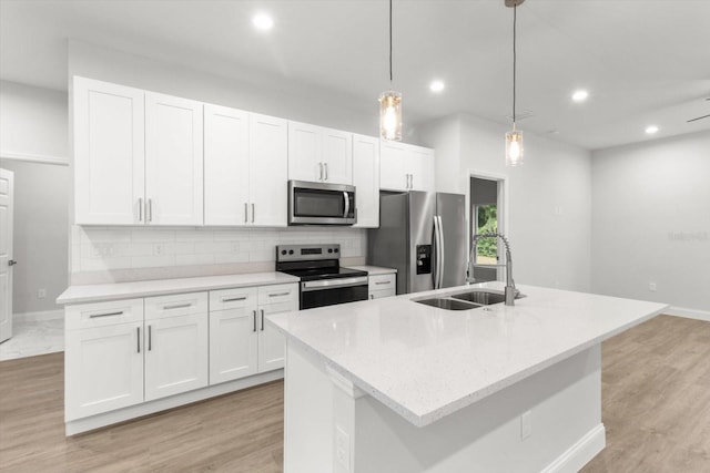 kitchen featuring decorative light fixtures, stainless steel appliances, white cabinetry, and a kitchen island with sink