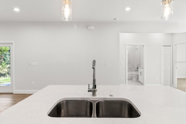 kitchen featuring decorative light fixtures, light stone counters, wood-type flooring, and sink