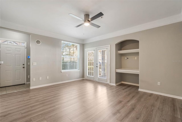 unfurnished living room with built in shelves, wood-type flooring, ceiling fan, and ornamental molding