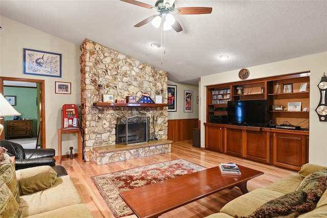 living room with a textured ceiling, light wood-type flooring, a fireplace, and vaulted ceiling