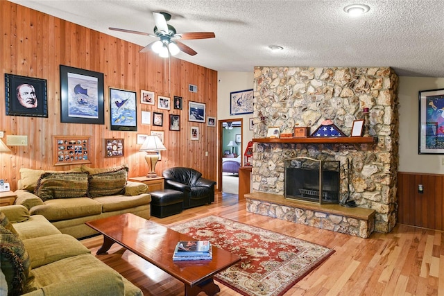 living room featuring lofted ceiling, a stone fireplace, hardwood / wood-style flooring, ceiling fan, and a textured ceiling