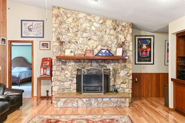 living room featuring a textured ceiling, a stone fireplace, light hardwood / wood-style flooring, and vaulted ceiling