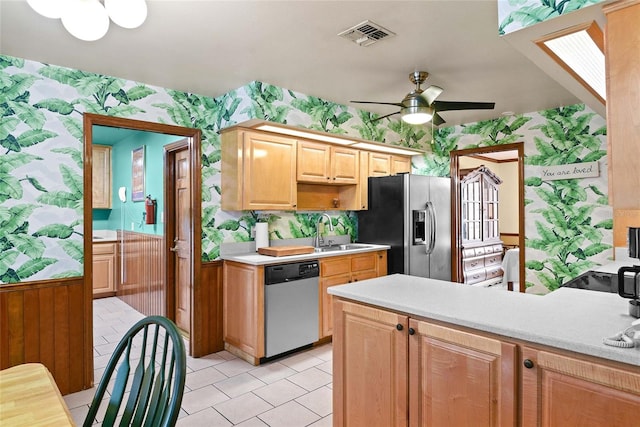 kitchen with ceiling fan, sink, stainless steel appliances, wooden walls, and light brown cabinetry