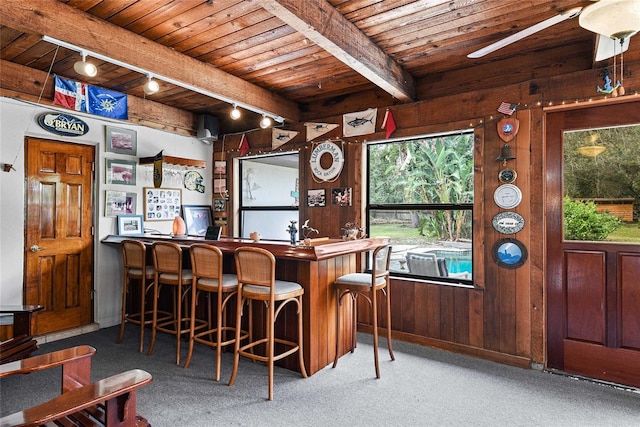 bar featuring ceiling fan, wooden ceiling, beamed ceiling, wood walls, and carpet