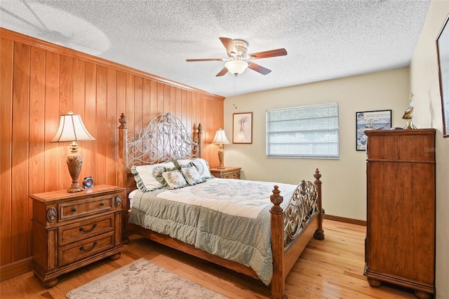 bedroom with ceiling fan, light hardwood / wood-style floors, a textured ceiling, and wooden walls