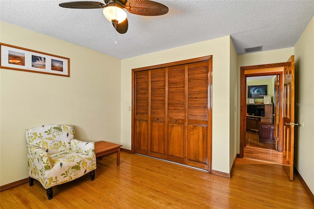 living area with a textured ceiling, light hardwood / wood-style floors, and ceiling fan